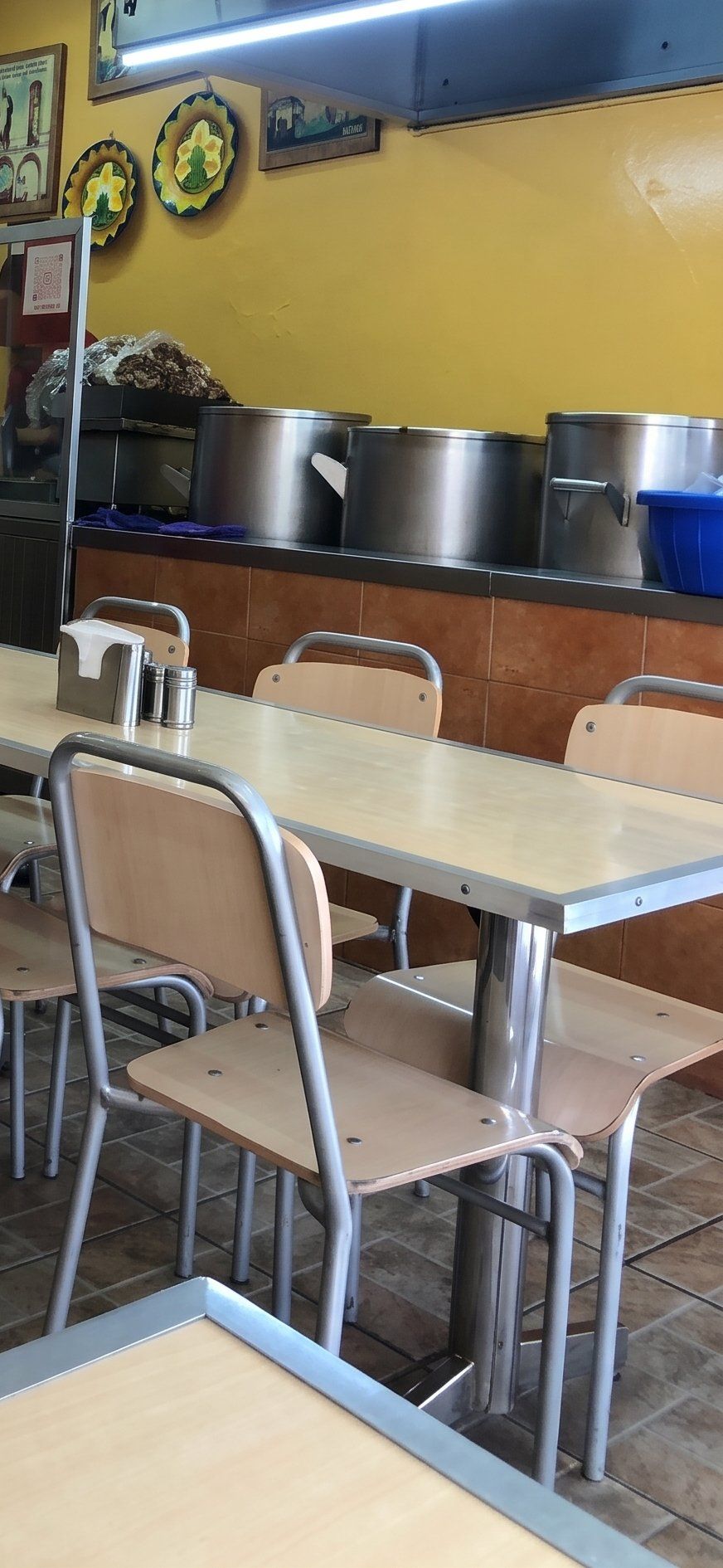 Mesas y sillas del comedor junto a la barra con ollas de acero
