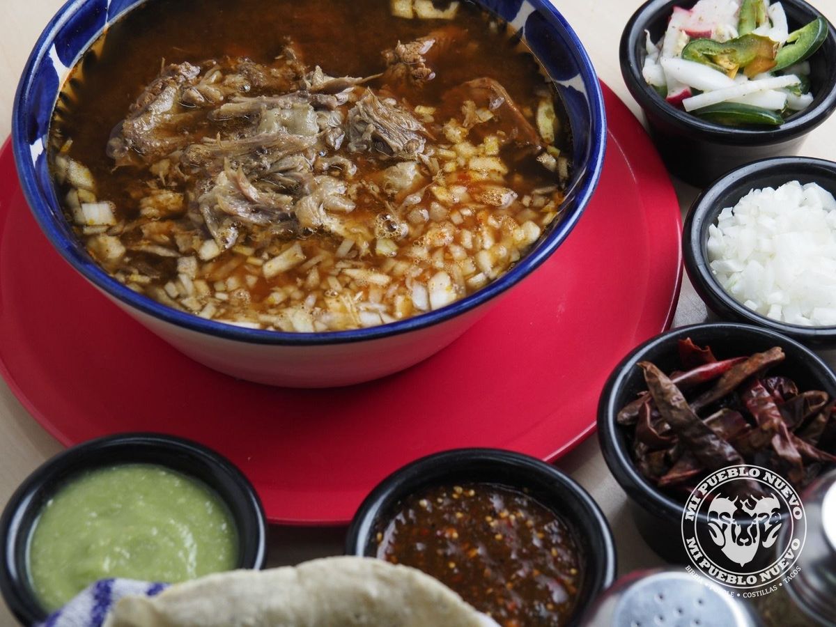 Tazón de birria de chivo con consomé, acompañado de cebolla, chiles y salsas