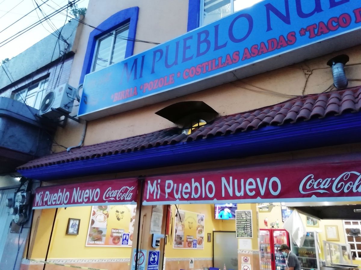 Fachada con el rótulo azul de Mi Pueblo Nuevo, tejado y lonas rojas