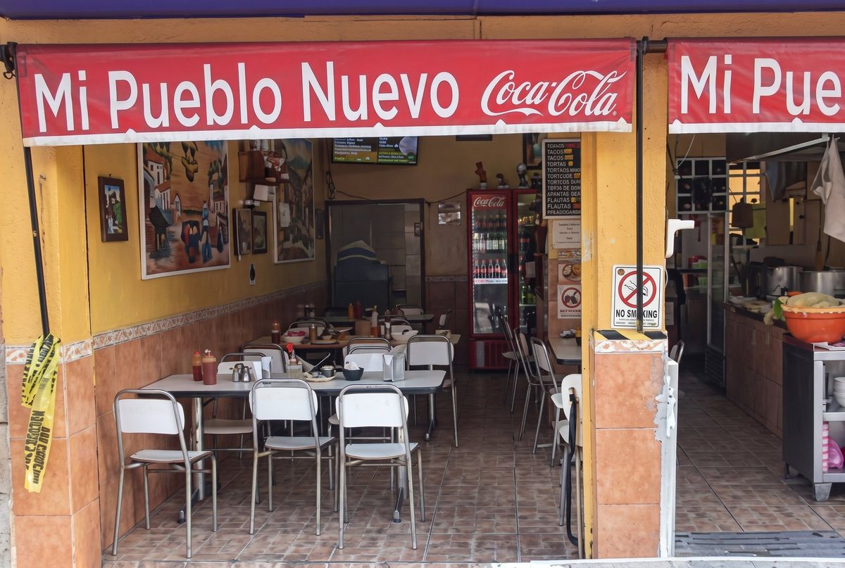 Entrada con lonas rojas y mesas del comedor vistas desde la calle
