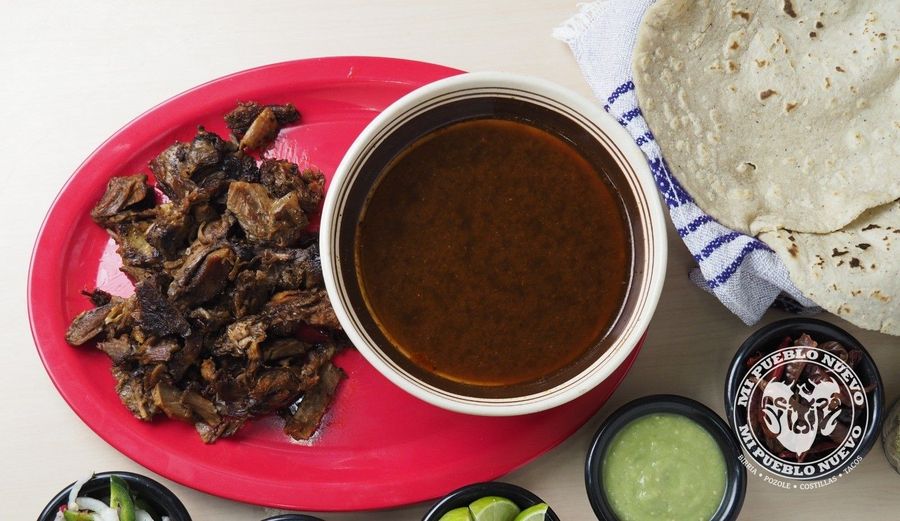 Plato de birria tatemada: carne de chivo dorada junto a un tazón de consomé y tortillas hechas a mano